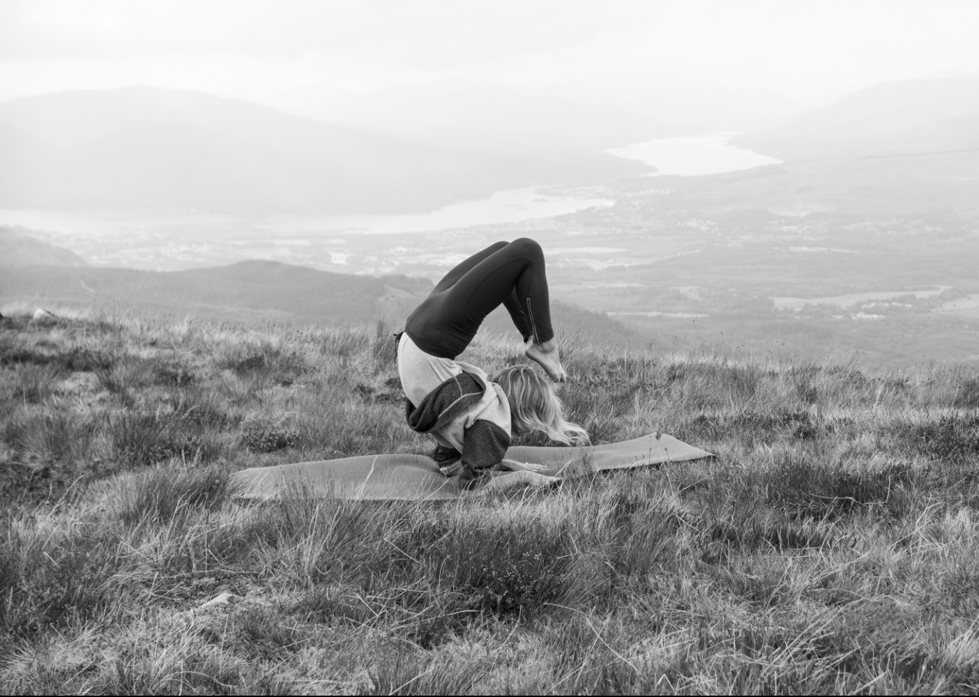 Woman practicing yoga in a field overlooking a valley